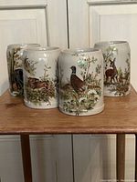 Front view of four ceramic beer steins each with different wildlife designs placed on a wooden surface.