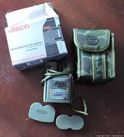 Jason Perma Focus 2000 binoculars with original box, camouflage carrying case, two lens caps, strap, and lens cloth arranged on a surface.