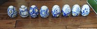 Set of eight porcelain decorative eggs arranged in a row, predominantly blue and white with floral patterns and some yellow flower centers.