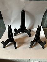 Three black wooden plate stands shown on white background, with varying sizes; medium and small stands visible.