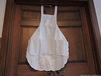 White apron with floral eyelet cutwork and scalloped bottom hanging on wooden door