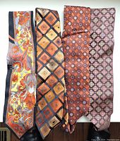 Four men's silk ties in orange/yellow tones laid flat to show patterns and colors including floral, diamond, and geometric designs.