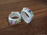 Two porcelain napkin rings with detailed pastel flower decorations on a wooden surface.