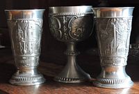 Photo showing three pewter cups: two with architectural reliefs and one chalice with hunting scene.