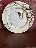 Top view of the porcelain plate featuring a stylized crane with pine tree artwork in black, gray and red accents.
