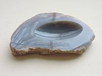 Top and angled view of polished agate ashtray showing translucent grey banded patterns and rough natural edge.