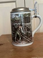 Porcelain beer stein showing a man pushing a beer cart with barrels, featuring a cast pewter lid with thumb lever