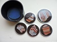 Top-down view of four round coasters with unique quartz inlays arranged next to a dark cylindrical storage container with lid and blue interior lining.