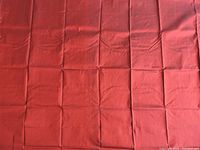 Raw silk fabric spread out showing its crimson color and visible crease lines from folding.