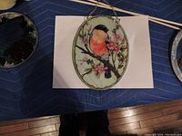 Oval stained glass window showing a bird with red chest sitting on a flowering branch with pink blossoms.