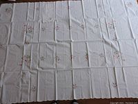 White tablecloth laid out showing pink embroidered floral pattern with diamond shapes.