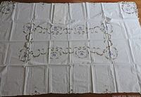 Full view of the white tablecloth laid out flat showing embroidered floral design and cutwork pattern