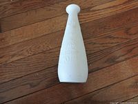 White porcelain vase with floral relief design, placed on wooden floor for display.