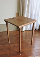 Vintage teak end table with square top and tapered legs on hardwood floor next to light curtains.