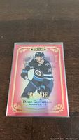 Front view of David Gustafsson rookie card in plastic sleeve showing player in Winnipeg Jets uniform with red and gold design.
