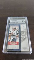 Clear protective slab with Tom Brady 2013 Panini Contenders football ticket showing action image and grading label with score 8.5.