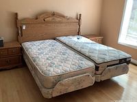 Front view of oak wood bed frame with two adjustable mattresses side by side showing floral and Serta mattress covers, footboards, and nightstands.