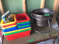 Stack of 12 plastic bins in red, yellow, blue, green colors on the left side and two metallic planters on the right side on a wooden surface.