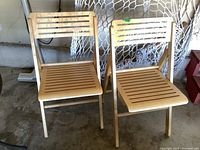 Two folding wood chairs placed side by side in a garage with visible wood slats on seat and backrest.