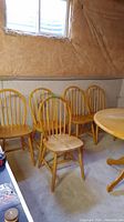 Five natural wood dining chairs grouped together in basement setting with concrete floor and unfinished walls.