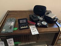 Full lot photo showing Xbox 360 hard drive, three cameras, digital alarm clock, multi-tool with red handle, and camera carrying cases.