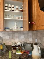 Shelves and counter with mixed dishware including ceramic mugs, glass bowls, plates, pitchers, and wooden items.