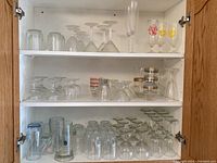 Three shelves of various types of glasses including wine glasses, cocktail glasses, champagne flutes, beer mugs, and tumblers.