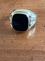 Front view of ring showing black rectangular onyx set in yellow gold bezel and sculpted shoulders