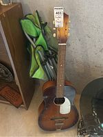 Full view of Winston acoustic guitar leaning against a wall next to green folding camp chair, showing guitar's wooden body and chair's fabric and frame.