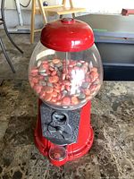 Front view of red Carousel gum ball machine with glass globe filled with gum balls on top and coin mechanism below.