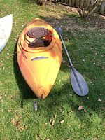 Orange Sunstream kayak resting on grass alongside paddle