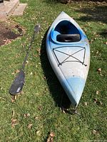Front three-quarter view of kayak and paddle on grass