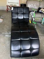 Front angled view of black vinyl lounge chair on concrete floor showing tufted cushion pattern and top surface wear.