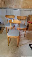 Three mid-century wooden chairs with vinyl seats arranged in basement with visible scratches and wear.
