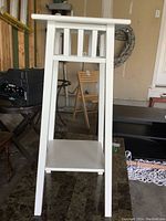 Front view of white wooden plant stand showing its rectangular top surface, four legs, and lower shelf.