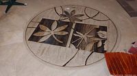 Full view of the round beige rug with brown and cream leaf pattern and curved line design.