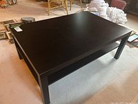 Black coffee table shown from a diagonal corner angle, highlighting the flat top surface and overall structure.