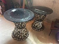 Pair of side tables shown in a basement setting with guitars in background. Tables have metal ruffled bases and smoked glass tops.