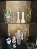 Two shelves of vases including milk glass, clear and colored glass, and ceramic pieces.