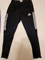 Front view of black Adidas track pants showing Adidas logo and white side stripes