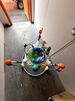Baby jumper activity center with colorful padded seat and multiple attached toys, shown from above in a hallway.