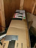 Cardboard box packaging with visible tape and a label showing an image of the packed Christmas tree.