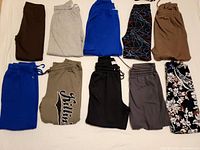 Top-down view of 10 pairs of folded sweatpants in various colors and patterns arranged in two rows.