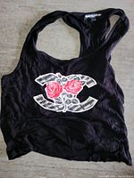 Front view of black women's tank top with Crooks and Castles graphic featuring two red roses on stylized 'C' logo with newspaper print