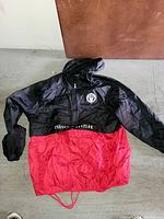 Full view of black and red men's windbreaker jacket laid flat showing color block design and hood.