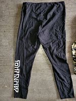 Black leggings with pink PINK logo print laid flat on a cement floor.