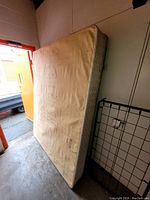 Queen size mattress shown standing upright indoors, beige fabric with some visible stains and wear on surface.