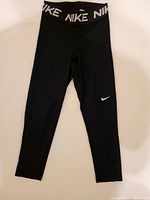 Full view of the black Nike women's leggings showing waistband with NIKE logo and white swoosh on left thigh.