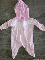 Pink Puma baby onezie with white chest detail, front zipper, hood, and footed legs laid flat on floor.