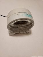 Front view of white fan heater showing air grill, control knob, and small wheels on base.